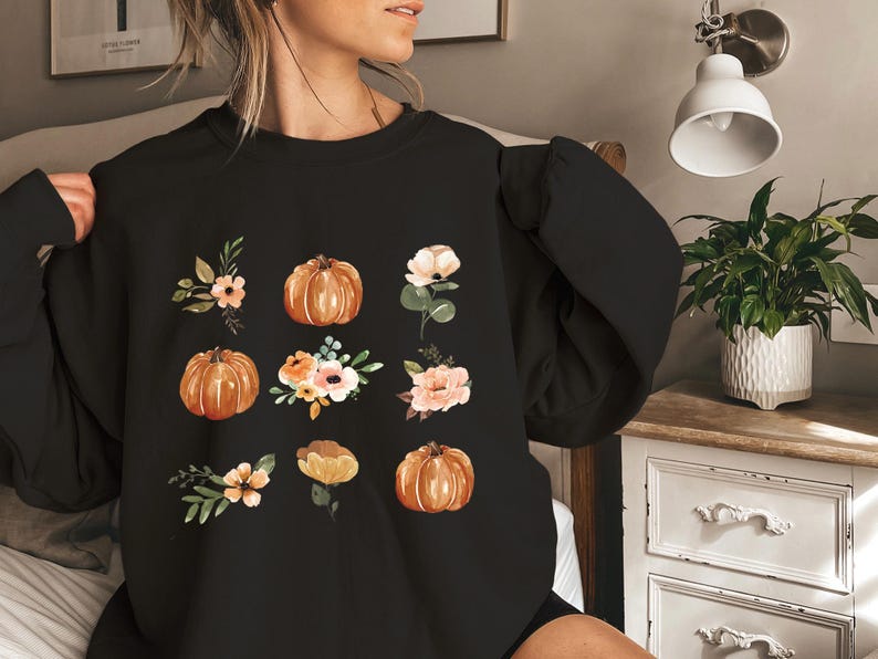 Puede incluir: Sudadera negra con ilustraciones en acuarela de calabazas y arreglos florales en tonos naranja, melocot&oacute;n y crema. El dise&ntilde;o es un patr&oacute;n con tem&aacute;tica oto&ntilde;al, perfecto para el oto&ntilde;o.