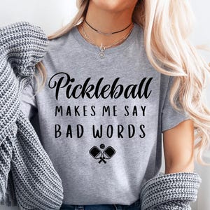 May include: Grey t-shirt with the text "Pickleball makes me say bad words" and a graphic of two pickleball paddles.