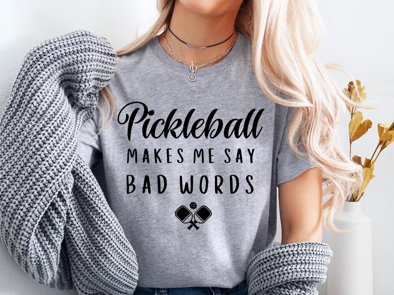 May include: Grey t-shirt with the text "Pickleball makes me say bad words" and a graphic of two pickleball paddles.