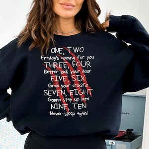 May include: Black sweatshirt with white text and red claw marks. The text reads "ONE, TWO Freddy's coming for you THREE, FOUR Better lock your door FIVE, SIX Grab your crucifix SEVEN, EIGHT Gonna stay up late NINE, TEN Never sleep again!"