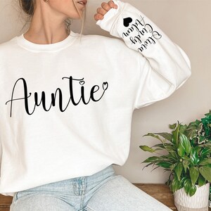 May include: White sweatshirt with the word "Auntie" and a small heart on the front. The sleeves have the words "Little" "Cousin" "Auntie" and a heart printed on them.