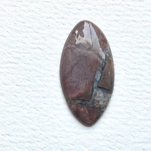May include: A polished, oval-shaped gemstone with a mix of burgundy, brown, and gray tones. The stone has a glossy finish and a natural, marbled appearance. This gemstone is suitable for jewelry making.
