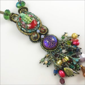 May include: A multi-colored beaded necklace with a green frog charm and a purple iridescent bead. The necklace has a long tassel of beads in various colors and textures.