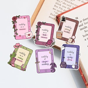 May include: A collection of colorful stickers with the phrase "mentally in" followed by various book genres. Designs include a cowboy romance, dark romance, spooky stories, and dragon academy themes. The stickers are rectangular with rounded corners.