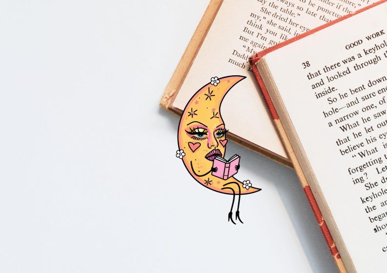 May include: A whimsical bookmark featuring a yellow crescent moon with a face, reading a pink book. The bookmark is decorated with hearts and flowers. Two open books are in the background.