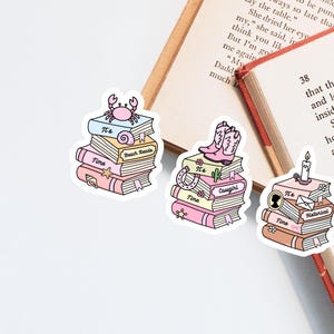 May include: Three die-cut stickers featuring stacks of books with pastel covers. One stack has a crab and seashell, one has pink cowboy boots and a cactus, and one has a candle and envelope. Each stack includes the text It's Time and a genre label.