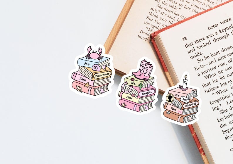 May include: Three die-cut stickers featuring stacks of books with pastel covers. One stack has a crab and seashell, one has pink cowboy boots and a cactus, and one has a candle and envelope. Each stack includes the text It's Time and a genre label.
