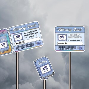 May include: A collection of light blue library cards and a book-shaped sticker with a spooky theme. The cards feature a ghost wearing a witch hat, the text "Spooky Book Club", and the phrase "the club of those who read books until they die".