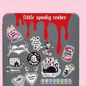 Pode incluir: Uma capa cinzenta para e-reader adornada com autocolantes com temas assustadores. Os autocolantes incluem frases como "Stay Spicy", "True Crime" e "Dark Romance". Um design vermelho gotejante com o texto "little spooky reader" est&aacute; no topo.