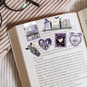 May include: A selection of Halloween-themed stickers in purple and white, placed on an open book. The stickers feature a coffin, a witch, a ghost, a bookshelf, and a heart design. The word "HORROR" is printed on one sticker.