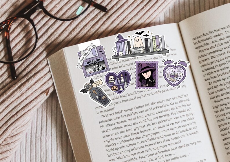 May include: A selection of Halloween-themed stickers in purple and white, placed on an open book. The stickers feature a coffin, a witch, a ghost, a bookshelf, and a heart design. The word "HORROR" is printed on one sticker.