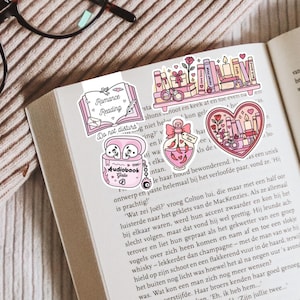May include: A collection of pink and white stickers with a romance reading theme, including a bookmark, a heart-shaped design, and a perfume bottle. The stickers are placed on the open pages of a book.