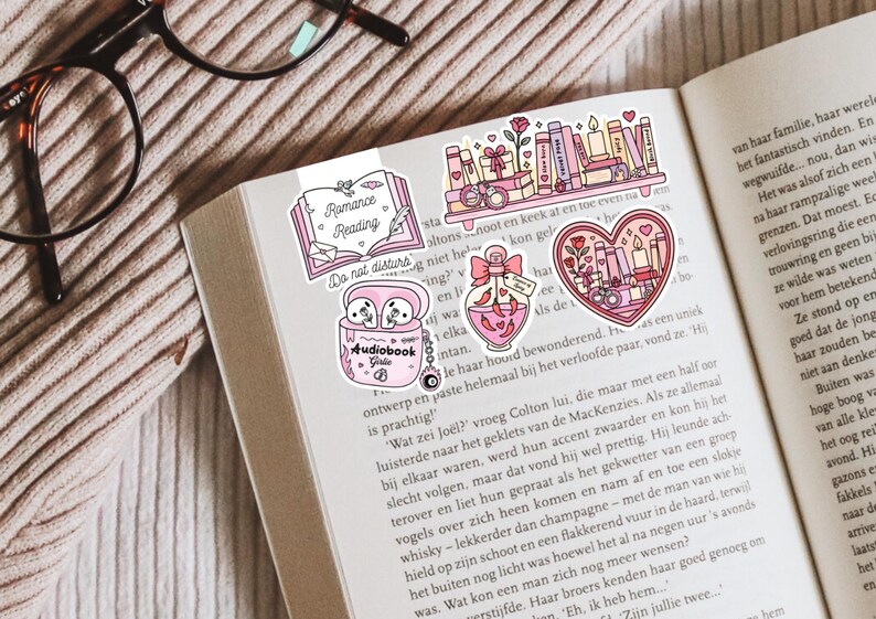 May include: A collection of pink and white stickers with a romance reading theme, including a bookmark, a heart-shaped design, and a perfume bottle. The stickers are placed on the open pages of a book.