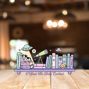 Op de afbeelding: Een grillige illustratie van een boekenplank met boeken, een telescoop en UFO's. De boeken hebben titels als "Interstellar" en "Galaxies". Een koe staat op een stapel boeken. De plank heeft de tekst "I Have No Shelf Control."