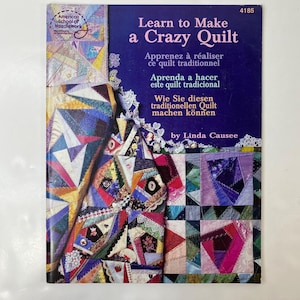 Peut inclure: Un livre d'instructions à couverture souple intitulé Learn to Make a Crazy Quilt par Linda Causee, présentant une couverture bleu foncé avec un grand motif de patchwork coloré affichant diverses textures de tissu, dentelle et broderies.