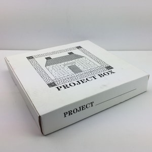 May include: A white project box with a black and white illustration of a house on the lid. The box has the words "PROJECT BOX" printed in black. The word "PROJECT" is also printed on the side of the box.