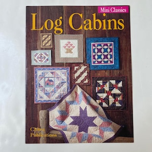May include: A book cover titled "Log Cabins" with various miniature quilt designs. The cover features a wooden background with the title in large yellow letters. The quilts showcase geometric patterns and a star design. The publisher is Chitra Publications.