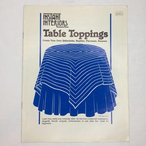 May include: A vintage book cover titled "Instant Interiors Table Toppings." The cover features a blue and white graphic of a tablecloth. The text reads, "Create Your Own Tablecloths, Napkins, Placemats, Runners." Additional text at the bottom.