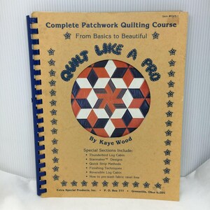 Puede incluir: Un libro encuadernado en espiral titulado "Complete Patchwork Quilting Course" con el texto "Quilt Like a Pro". La portada presenta un diseño de edredón geométrico en rojo, blanco y azul. El libro incluye secciones especiales sobre técnicas de acolchado.