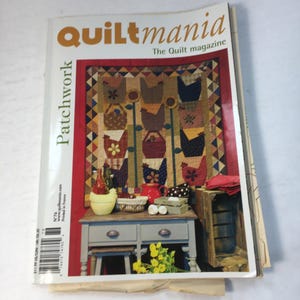 May include: A stack of magazines, the top one titled "QUILtmania" in orange. The cover shows a patchwork quilt with chicken motifs. The word "Patchwork" is printed vertically on the left. The magazine is a quilt magazine.