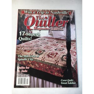 Puede incluir: Portada de la revista The Quilter, con un edredón en una cama. El título de la revista está en rojo y blanco. El texto de la portada incluye "17 Superb Quilts!" y "Cover Quilt: Sweet Adeline."