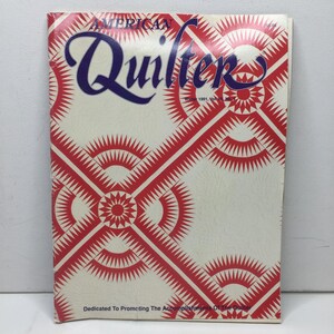 May include: The cover of the "American Quilter" magazine, featuring a cream background with a red geometric pattern. The magazine title is in a dark blue script. The text "Winter 1991, Vol. 2, No. 3" is also visible.