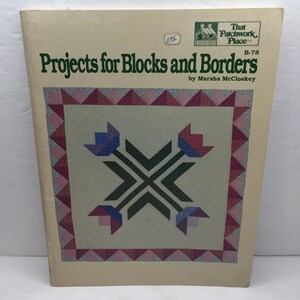 May include: A vintage book titled "Projects for Blocks and Borders" by Marsha McCloskey. The cover features a quilt design with blue and red floral motifs and a pink and red border. The book is cream-coloured with green text.