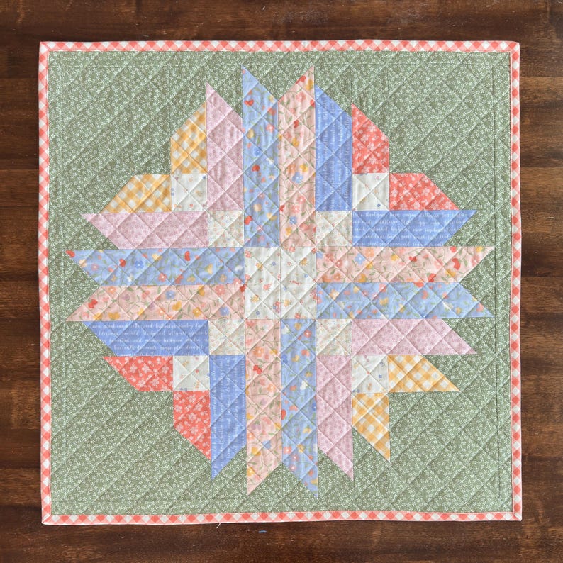 Pu&ograve; includere: Una trapunta quadrata fatta a mano con un motivo a stella. La trapunta presenta un motivo a stella centrale in tessuti rosa pastello, blu, gialli e bianchi. La stella &egrave; ambientata su uno sfondo verde con un motivo a diamante e un bordo a quadretti rossi e bianchi.