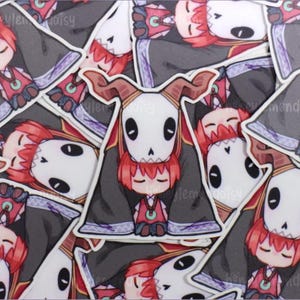 May include: A selection of stickers depicting a character with red hair and a white skull mask. The character is dressed in a black robe with red and purple details. The stickers are arranged in a random pattern.