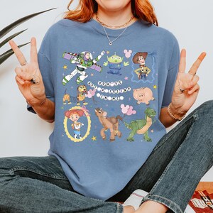 May include: A blue t-shirt featuring cartoon characters from the movie Toy Story. The shirt has a graphic design with Buzz Lightyear, Woody, and other characters. The text "You've Got a Friend in Me" is also displayed.