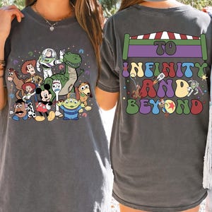 May include: Dark gray t-shirt featuring a colorful graphic of Toy Story characters, including Woody, Buzz Lightyear, and Rex. The back of the shirt displays the phrase "To Infinity and Beyond" in a retro font, with a rocket ship and other Toy Story characters.
