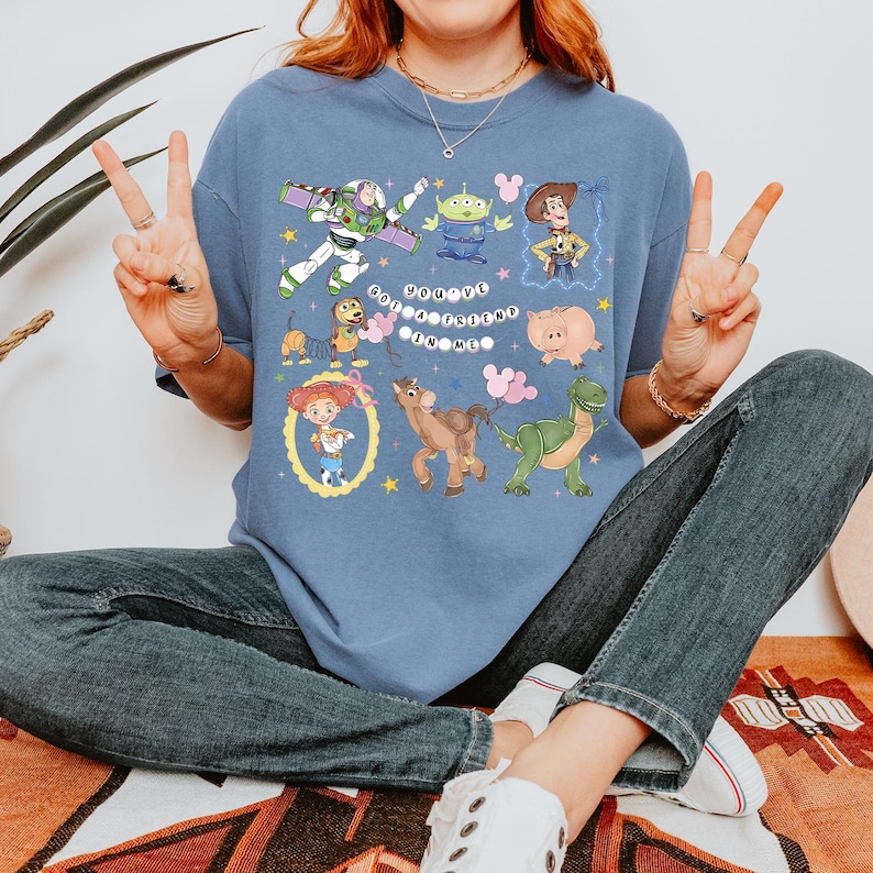 May include: A blue t-shirt featuring cartoon characters from the movie Toy Story. The shirt has a graphic design with Buzz Lightyear, Woody, and other characters. The text "You've Got a Friend in Me" is also displayed.