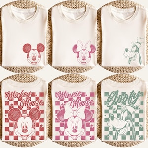 Puede incluir: Camisetas color crema con dise&ntilde;os de Mickey Mouse, Minnie Mouse y Goofy. Las camisetas de Mickey Mouse tienen gr&aacute;ficos rojos, las camisetas de Minnie Mouse tienen gr&aacute;ficos rosas y las camisetas de Goofy tienen gr&aacute;ficos verdes. Algunas camisetas tienen caras de personajes, otras tienen dise&ntilde;os completos con texto.