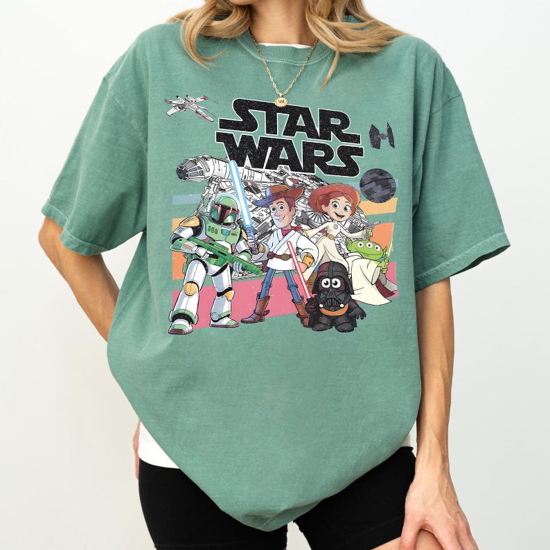 Puede incluir: Camiseta verde salvia con un gr&aacute;fico de Star Wars con personajes de dibujos animados y el logotipo de Star Wars. El dise&ntilde;o incluye personajes como Darth Vader, Woody y Buzz Lightyear. La camiseta tiene un corte holgado.