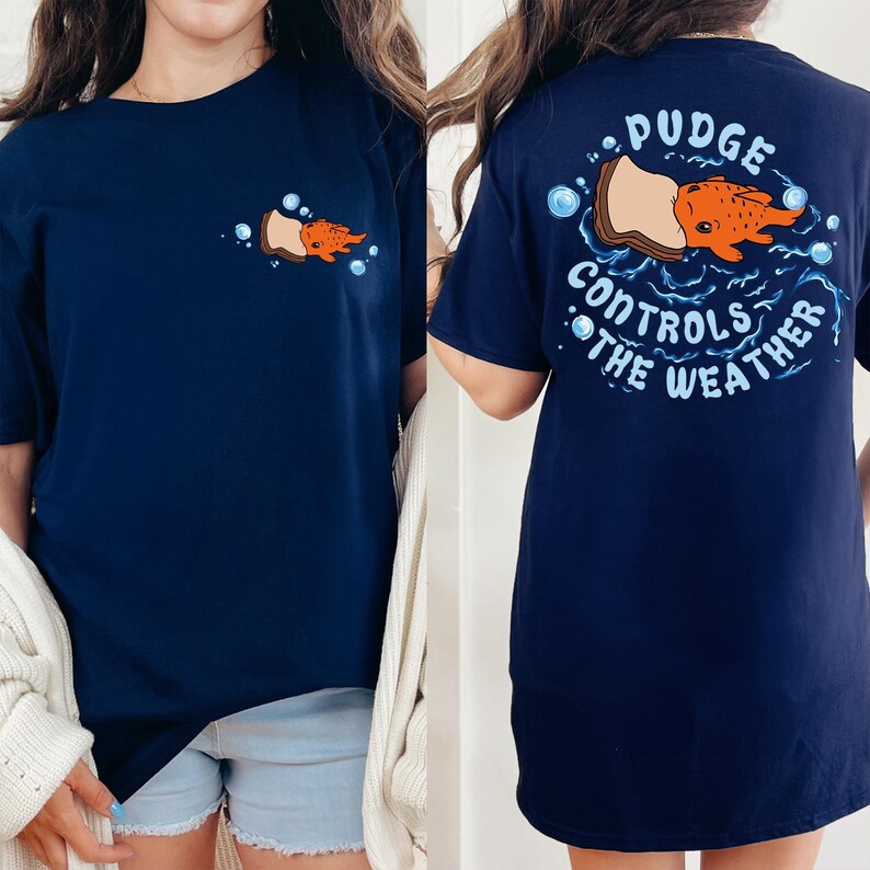 May include: Navy blue t-shirt with a cartoon illustration of a fish on a sandwich, with bubbles. The back of the shirt has the text "Pudge Controls the Weather" in a circular design around the same fish illustration.