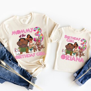 Op de afbeelding: Twee cr&egrave;mekleurige T-shirts met een cartoonafbeelding met personages uit een populaire animatiefilm. E&eacute;n shirt zegt "Mommy of the Birthday Girl" en de andere zegt "Birthday Girl Oriana" met het nummer 3.