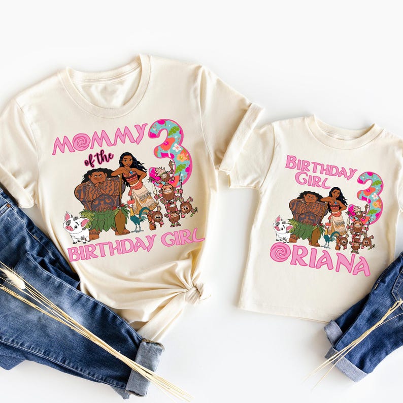 Op de afbeelding: Twee cr&egrave;mekleurige T-shirts met een cartoonafbeelding met personages uit een populaire animatiefilm. E&eacute;n shirt zegt "Mommy of the Birthday Girl" en de andere zegt "Birthday Girl Oriana" met het nummer 3.