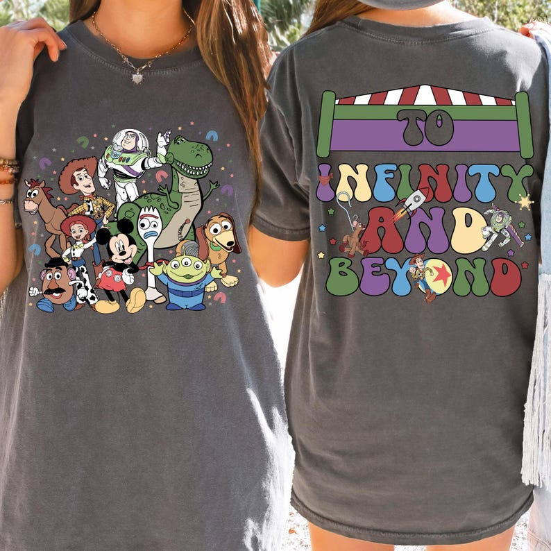 May include: Dark gray t-shirt featuring a colorful graphic of Toy Story characters, including Woody, Buzz Lightyear, and Rex. The back of the shirt displays the phrase "To Infinity and Beyond" in a retro font, with a rocket ship and other Toy Story characters.