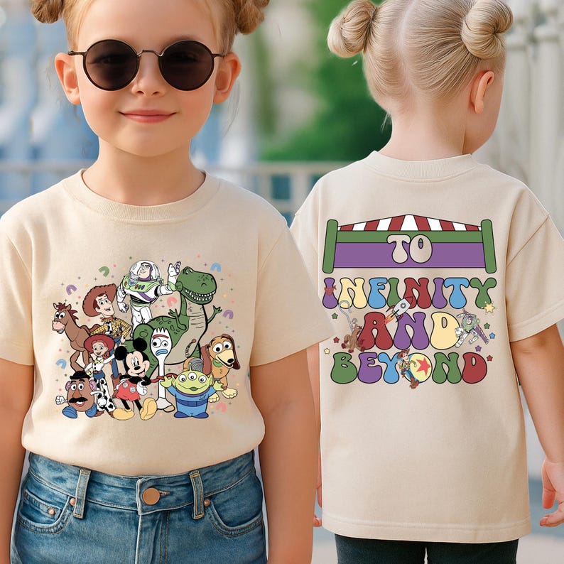 May include: Beige t-shirt featuring a colorful graphic of various cartoon characters. The front of the shirt displays a group of characters, while the back has the phrase "To Infinity and Beyond" in a retro font.