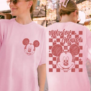Puede incluir: Camiseta rosa claro con un dise&ntilde;o desgastado de Mickey Mouse en la parte delantera y trasera. El dise&ntilde;o trasero incluye las palabras "Mickey Mouse" sobre un patr&oacute;n de cuadros con estrellas. Un dise&ntilde;o cl&aacute;sico y divertido.