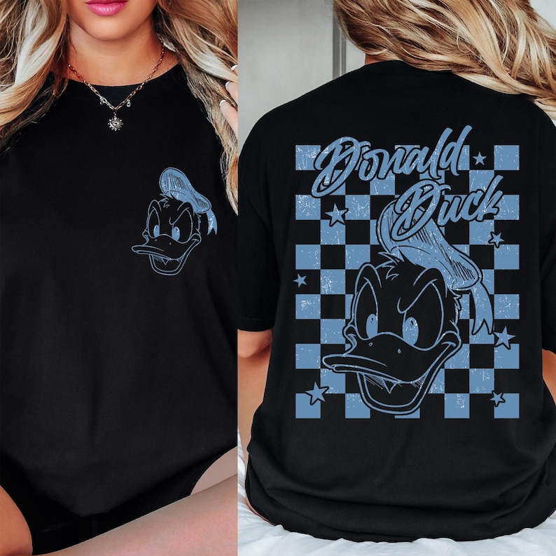 Puede incluir: Camiseta negra con un dise&ntilde;o de Pato Donald en azul claro en la parte delantera y trasera. El dise&ntilde;o trasero incluye las palabras "Donald Duck" y un patr&oacute;n de cuadros azules y blancos.