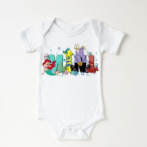 Puede incluir: Body de beb&eacute; blanco con la palabra "MIMI" en letras coloridas de estilo caricatura. Las letras est&aacute;n decoradas con personajes de una popular pel&iacute;cula animada, incluyendo una sirena, un pez y un cangrejo.