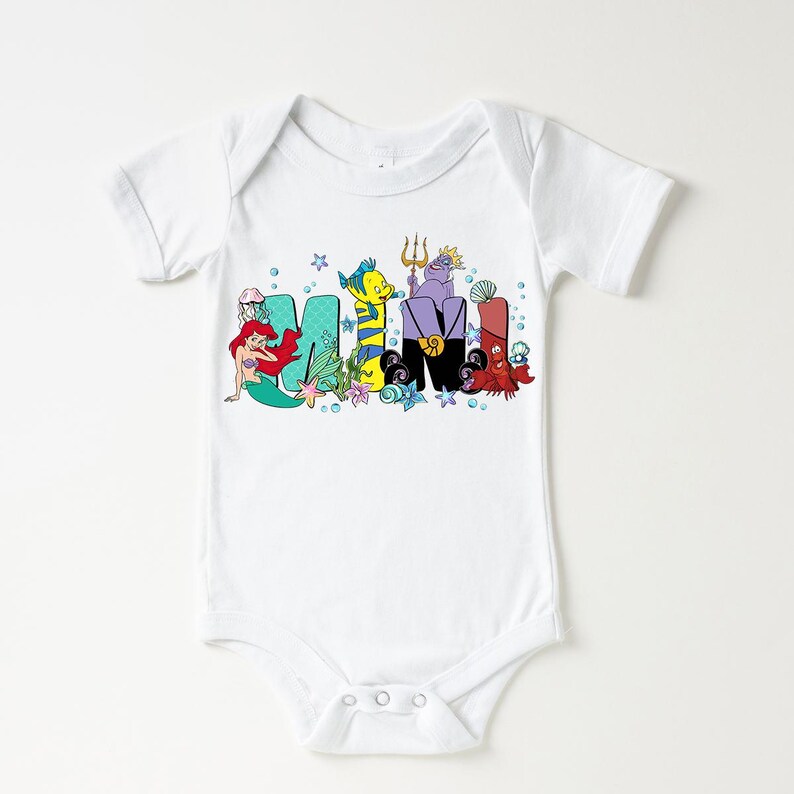 Puede incluir: Body de beb&eacute; blanco con la palabra "MIMI" en letras coloridas de estilo caricatura. Las letras est&aacute;n decoradas con personajes de una popular pel&iacute;cula animada, incluyendo una sirena, un pez y un cangrejo.