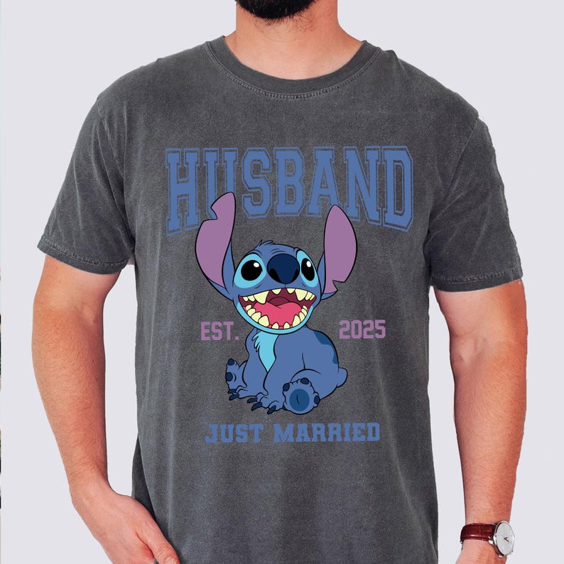 Puede incluir: Camiseta gris oscuro con un personaje de dibujos animados azul y la palabra "HUSBAND" en letras azules. La camiseta tambi&eacute;n presenta el texto "EST. 2025" y "JUST MARRIED" debajo del personaje.
