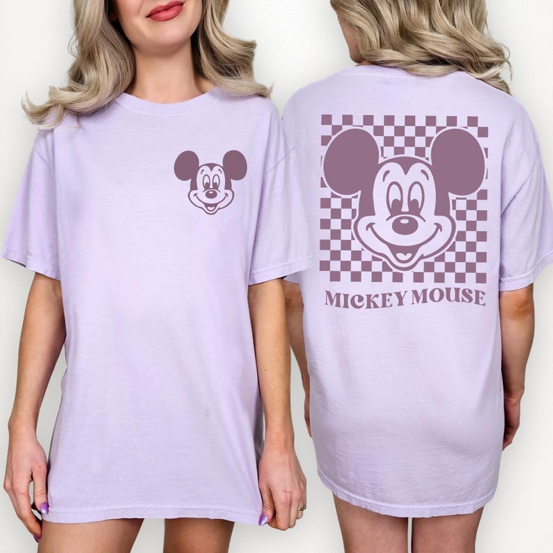 May include: A light purple t-shirt featuring a Mickey Mouse graphic on the front and back. The front has a small Mickey Mouse face, while the back has a larger Mickey Mouse face on a checkered background with the words "Mickey Mouse" below.