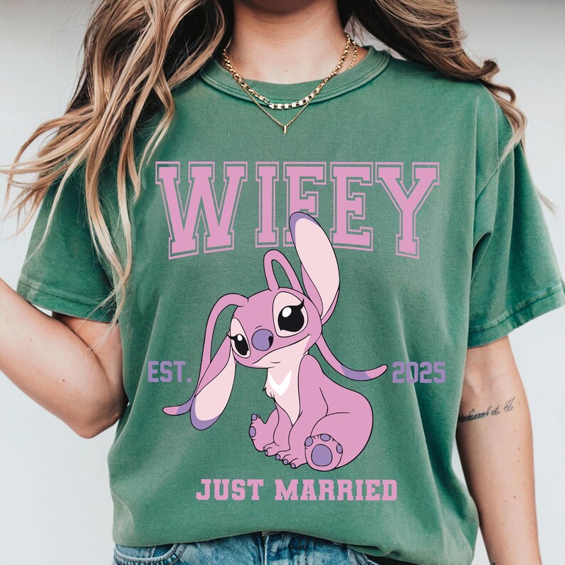 Puede incluir: Camiseta verde con la palabra "Wifey" en letras rosas en bloque sobre un personaje de dibujos animados rosa. Debajo del personaje, las palabras "Just Married" est&aacute;n impresas en rosa. El a&ntilde;o "2025" est&aacute; impreso a la derecha del personaje.