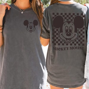May include: Gray t-shirt featuring a Mickey Mouse graphic on the front and back. The front has a small Mickey Mouse face, while the back showcases a larger design with a checkered background and the text "MICKEY MOUSE".