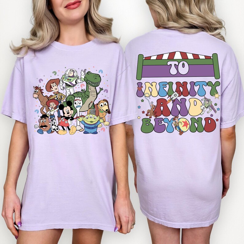 May include: A light purple t-shirt featuring a colorful graphic of Toy Story characters on the front. The back of the shirt has the text "To Infinity and Beyond" in a retro font, with a rocket ship and other graphics.