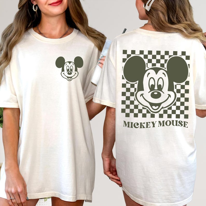 May include: Cream-colored t-shirt featuring a Mickey Mouse graphic. The front displays a small Mickey Mouse design, while the back showcases a larger Mickey Mouse design within a checkered pattern, with the words "MICKEY MOUSE" below.