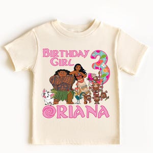 Op de afbeelding: Cr&egrave;mekleurig peuter-T-shirt met een kleurrijke afbeelding van tekenfilmfiguren. Het ontwerp bevat de tekst "BIRTHDAY GIRL" en het nummer "3" in roze, samen met een naam. Een leuk en feestelijk verjaardags-T-shirt.
